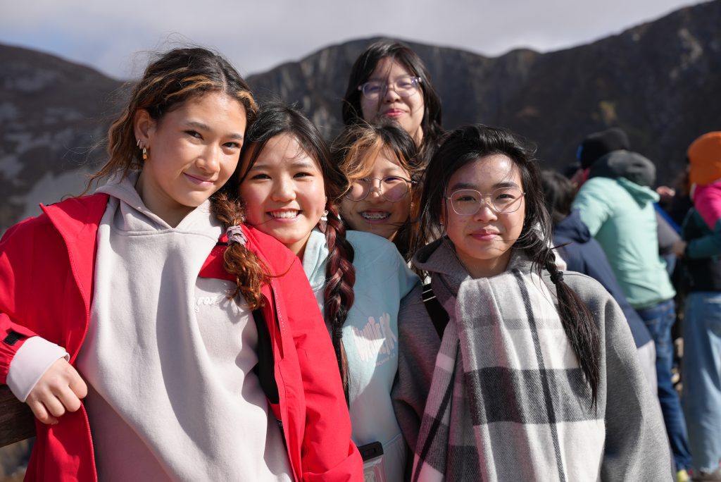 Five friends posing for a photo outdoors on a mountain with smiles.